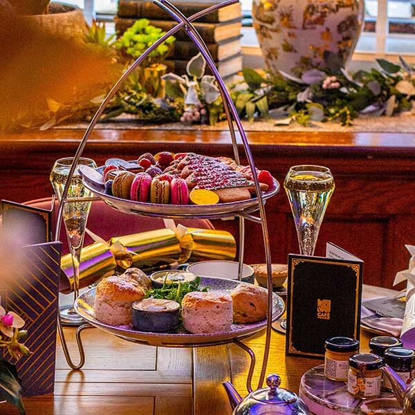 2 tiered Afternoon Tea stand with festive treats on both layers. 2 glasses of champagne are placed behind.