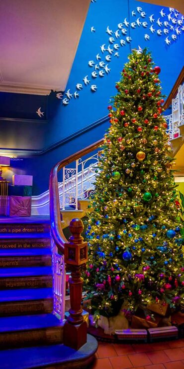 Christmas tree with coloured baubles next to stairs leading up to the first floor.